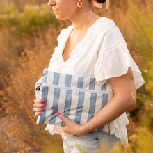 Load image into Gallery viewer, A woman in white blouse holds a Roamio by Bumkins Wet/Dry Clutch: Nautical Stripe among dry grass outdoors in golden sunlight.
