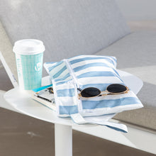 Load image into Gallery viewer, A Roamio by Bumkins Wet/Dry Clutch: Nautical Stripe with sunglasses & books sits on a table next to a coffee cup by a gray cushioned chair.