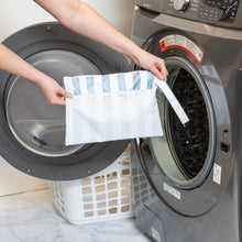 Load image into Gallery viewer, A person holds Roamio by Bumkins Wet/Dry Clutch: Nautical Stripe in front of an open front-loading washing machine.