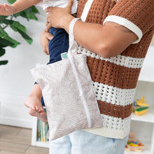 Load image into Gallery viewer, A person holds a child and a Bumkins Wet/Dry Clutch: Wander, dressed in a stylish brown and white knit top and jeans.