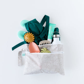Bumkins Wet/Dry Clutch: Wander on white background with a swimsuit, turquoise shoes, sippy cup, sunscreen, and toys.