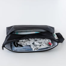 Load image into Gallery viewer, A compact Bumkins Wet/Dry Clutch: Black, slightly open to reveal clothes and diapers on a white background.