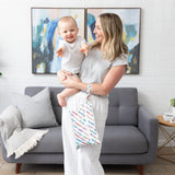 A woman holds a smiling baby and a Bumkins Wet/Dry Clutch: Mickey & Friends Varsity in a cozy living room.