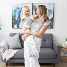 Load image into Gallery viewer, A woman holds a smiling baby and a Bumkins Wet/Dry Clutch: Mickey & Friends Varsity in a cozy living room.