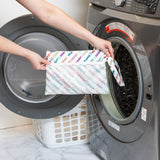 A person holds Bumkins Wet/Dry Clutch: Mickey & Friends Varsity in front of an open front-loading washing machine.
