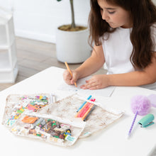 Load image into Gallery viewer, A girl draws at a white table with colored markers and a fluffy pen, near Bumkins Clear Travel Bag 3 Pack: Palm Daze filled with toy blocks.