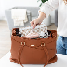 Load image into Gallery viewer, A person places a Roamio by Bumkins Clear Travel Bag 3 Pack: Sand Check with electronics in a brown purse on a white table.