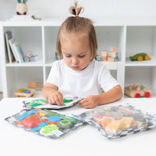 Load image into Gallery viewer, A child with a small ponytail sits at a white table with Bumkins Clear Travel Bag 3 Pack: Charcoal Check filled with toy blocks.