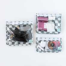 Load image into Gallery viewer, Bumkins Clear Travel Bag 3 Pack: Charcoal Check holds essentials like a hairbrush, toiletries, snacks, and earbuds on a white background.