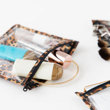 Load image into Gallery viewer, Close-up of Roamio by Bumkins Clear Travel Bag 3 Pack: Leopard with travel-size toiletries and makeup on a white background.