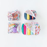 Bumkins Clear Travel Bag 3 Pack: Boots, filled with toiletries and cosmetics, sits next to organizers filled with clothes on a white background.