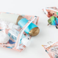 Load image into Gallery viewer, Close-up of Bumkins Clear Travel Bag 3 Pack: Yoga Pals holding travel-sized bottles, sunglasses, and hair accessories on a white background.