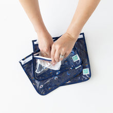 Load image into Gallery viewer, A person uses a wipe to clean the inside of Bumkins Clear Travel Bag 3 Pack: Evil Eye on a white table.