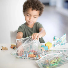 Load image into Gallery viewer, A curly-haired child opens Bumkins Clear Travel Bag 3-Pack: Cacti filled with toys in a bright room at a white table.