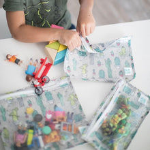 Load image into Gallery viewer, A child sits with Bumkins Clear Travel Bag 3-Pack: Cacti filled with toys on a white table.