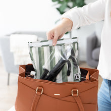Load image into Gallery viewer, A person places a Roamio by Bumkins Clear Travel Bag 3 Pack: Clubhouse Stripe with a camera tripod in a brown purse.