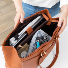 Load image into Gallery viewer, A person opens a brown purse on a white table, revealing notebooks and a Roamio by Bumkins Clear Travel Bag 3 Pack: Shells inside.