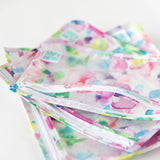 Close-up of Bumkins Clear Travel Bag 3-Pack: Watercolor stacked on a white background, with the top back unzipped, revealing the interior.