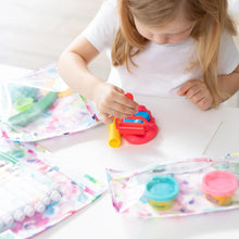 Load image into Gallery viewer, A young child sits at a table playing with colorful play dough, surrounded by art supplies in Bumkins Clear Travel Bag 3-Pack: Watercolor.