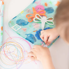 Load image into Gallery viewer, Close-up of a child zipping a Bumkins Clear Travel Bag 3-Pack: Ocean Life filled with art supplies next to a colorful doodle.
