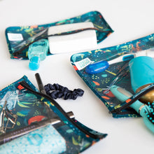 Load image into Gallery viewer, Close-up of Bumkins Clear Travel Bag 3-Pack: Jungle with toiletries and makeup on a white background.