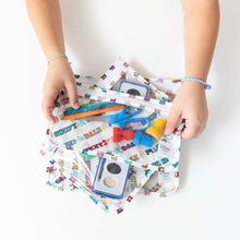 Load image into Gallery viewer, A child holds Bumkins Clear Travel Bag 3 Pack: Mickey & Friends Varsity filled with art supplies at a white table.
