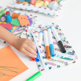 A child's hand reaches for markers from Bumkins Clear Travel Bag 3 Pack: Mickey & Friends Varsity on a table, surrounded by art supplies.
