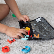 Load image into Gallery viewer, Close-up of a child reaching for letter-shaped magnets from a Bumkins Clear Travel Bag 3-Pack: Mickey Mouse Icon Black + White.