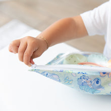 Load image into Gallery viewer, A child with a bracelet unzips a Bumkins Clear Travel Bag 3 Pack: Aloha Stitch at a white table.