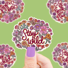 Load image into Gallery viewer, Hand holding Turtle Soups Stay Wild durable vinyl sticker featuring floral patterns on a green background.