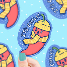 Load image into Gallery viewer, A Its Chili Pepper Cold Turtle Soup sticker shows a chili in a hat and scarf on blue, held by teal-nailed hand. Durable, waterproof vinyl!.