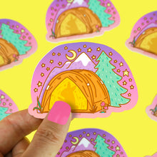 Load image into Gallery viewer, A hand holds Turtle Soups Vinyl Sticker, Camping Tent, featuring a crescent moon and starry sky over a yellow tent with mountains and a pine tree. The colorful, scratch-resistant, waterproof design repeats on a bright yellow surface.
