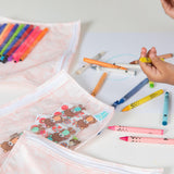 Close-up of a child at a white table, surrounded by crayons and Bumkins Clear Travel Bag 3-Pack: Lace with art supplies.