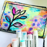 Hand holding vibrant Life of Colour Pastel Gouache Paint Stix; create abstract leaves and circles mess-free on a painted background.