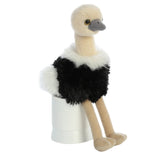 Aurora's Mini Flopsie Ozzi plush sits adorably on a white cylinder, facing left—perfect for animal lovers!.