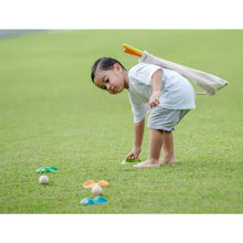 Load image into Gallery viewer, A child plays on the grass with a PlanToys Mini Golf Set, arranging colorful cones and balls, toy bag slung over their shoulder.