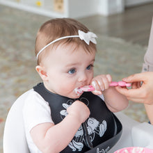 Load image into Gallery viewer, Close-up of an adult hand feeding a baby wearing a black bib with a Bumkins Silicone Dipping Spoons: Minnie Mouse (Black and Pink).
