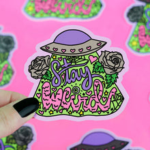 Load image into Gallery viewer, The Turtle Soup Stay Weird vinyl sticker features vibrant text, a hat, roses, hearts, and greenery held by a hand with black nails.

