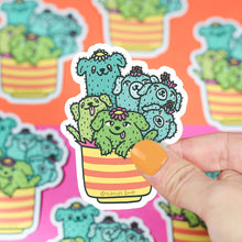 Load image into Gallery viewer, Hand holds a Turtle Soup Vinyl Sticker, Cactus Pups design; cute and durable with more premium vinyls in the background.
