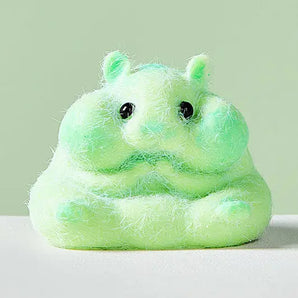 The Showcase SqueezeSquad Green Hamster Squishy with big black eyes sits on a white surface against a pale green background.