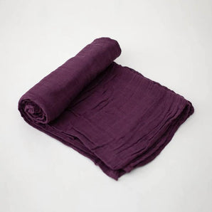 The Little Unicorn Cotton Swaddle in Plum rests on white, ready to wrap your baby in soft comfort.