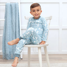 Load image into Gallery viewer, A child smiles in Tesa Babes Wild West Blue PJs while a textured blue blanket drapes over a nearby ladder.
