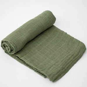 A Little Unicorn Cotton Swaddle in Fern is rolled up on one end and laid flat on a white surface.