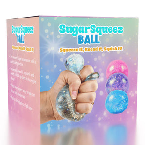 A hand squeezes a Sugarsqueez Glitter Ball by Showcase, with three colorful balls and product text on a pastel rainbow box.
