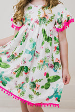 Load image into Gallery viewer, Girl in Mila and Rose’s Pom Pom Dress, Cute Cactus—ideal for a fun playground day with its floral print and pink pom-pom trim.

