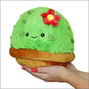 A person holds a Mini Cactus Plush by Squishable, shaped like a happy green cactus with a red flower in a brown pot.