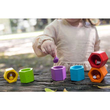 Load image into Gallery viewer, A child plays outdoors on a wooden surface with PlanToys Beehives, enhancing fine motor skills and color recognition.
