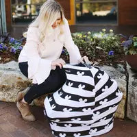 Load image into Gallery viewer, A woman sits on a stone ledge, draping a Milk Snob multifunctional cover with Disneys Mickey Mouse over an object, flowers blooming nearby.

