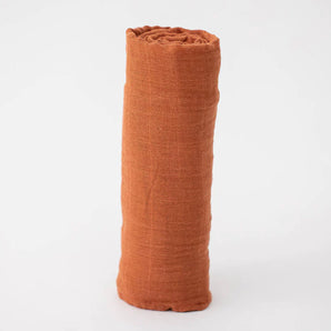 Little Unicorn Cotton Swaddle in rust stands rolled upright on a white background.