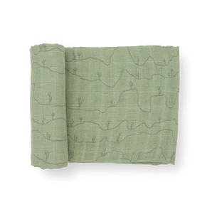 Little Unicorn's Cotton Swaddle, Cactus Lines: green cotton muslin with desert hills and cacti line art, shown partially rolled.
